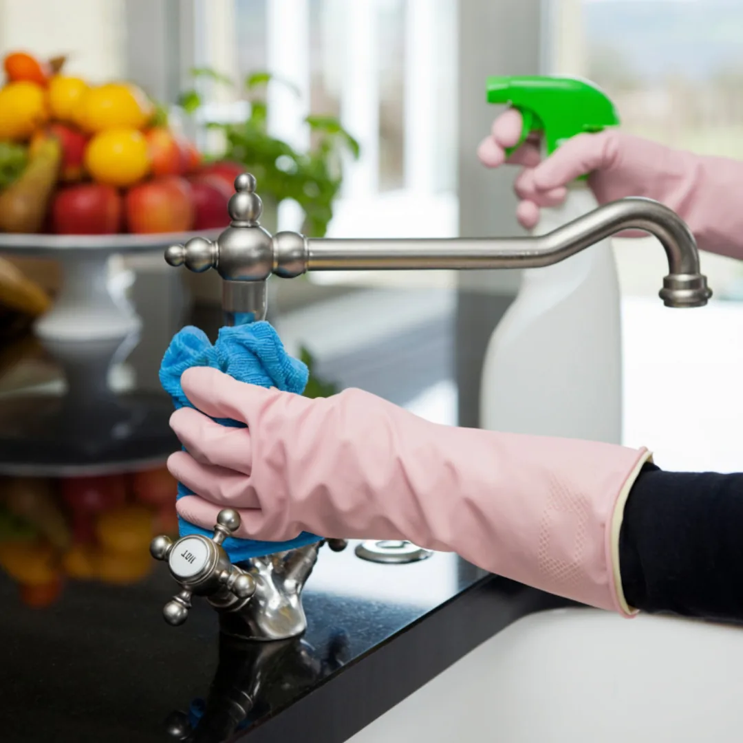 Gloved hands cleaning a kitchen faucet with blue cloth
