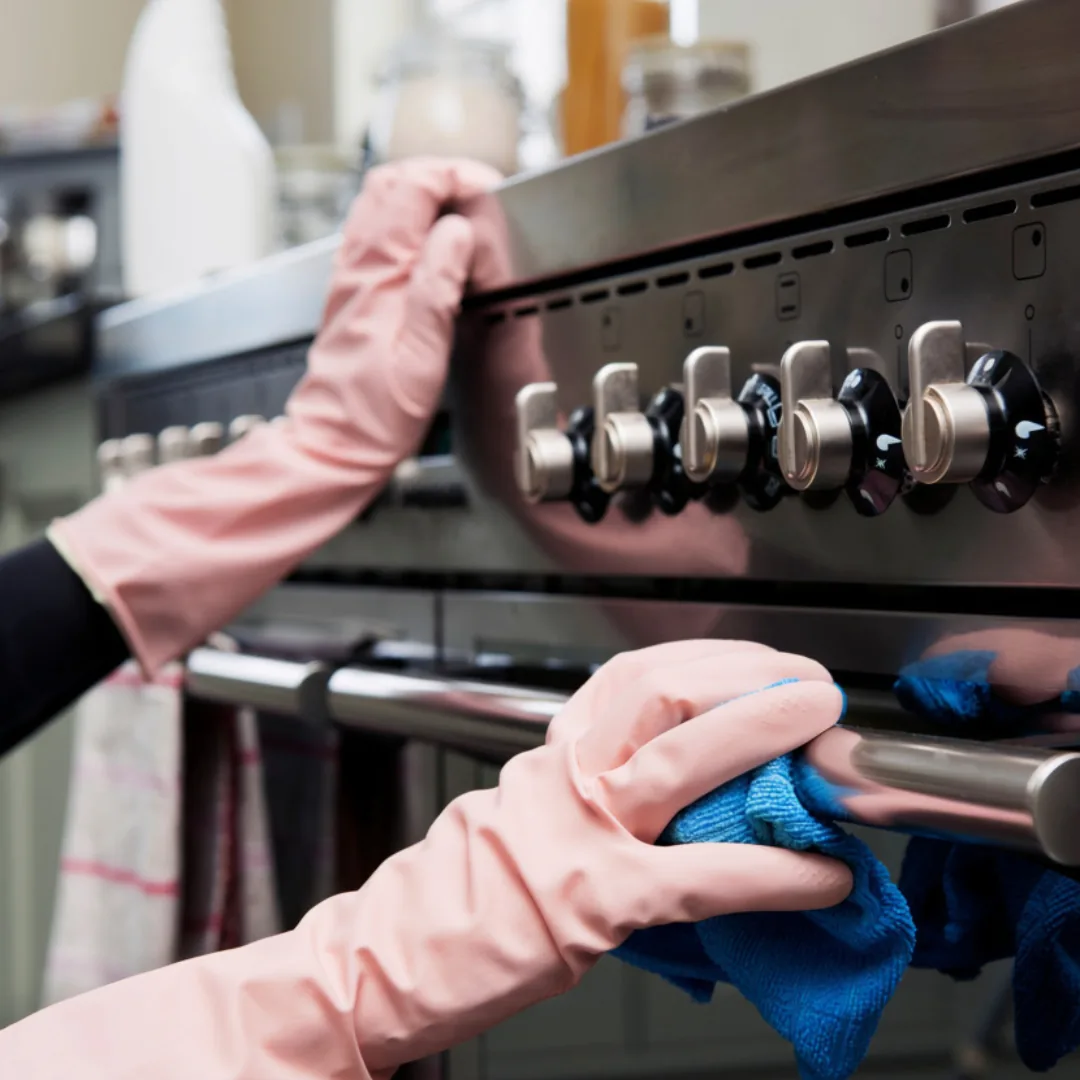 Gloved hands cleaning a stainless steel oven.