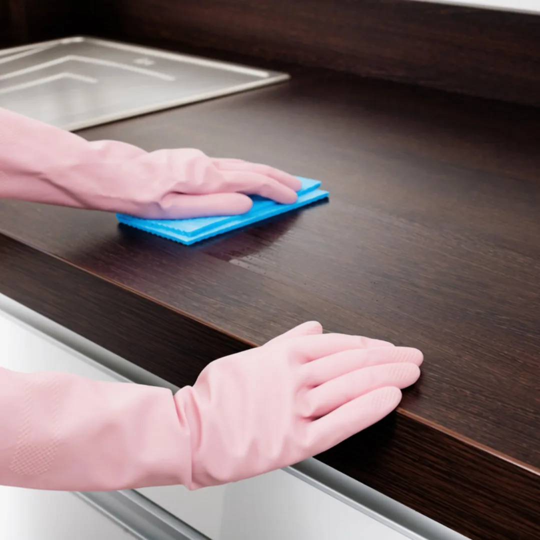 Gloved hands wiping down dark wood kitchen counter