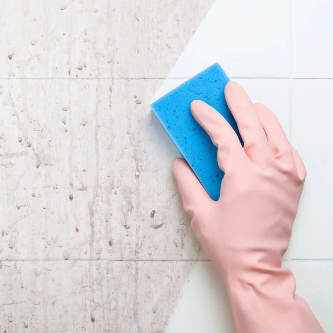 Hand in pink glove cleaning dirty tiles with blue sponge